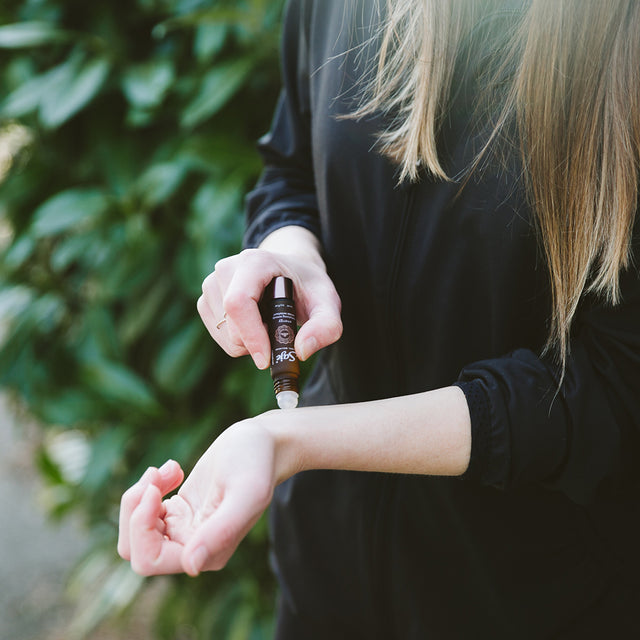 A woman applying a roll-on to a pulse point on the inside of the wrist
