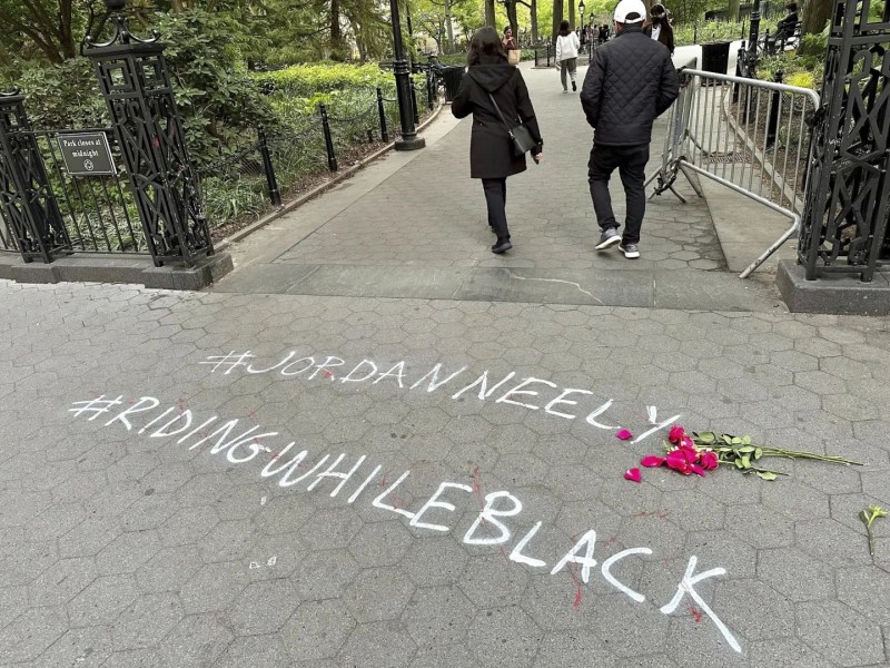 People walk past graffiti calling attention to death of Jordan Neely that was painted on the sidewalk at an entrance to Washington Square Park, Friday, May 5, 2023, in New York. Neely, a locally-known Michael Jackson impersonator who friends say suffered from worsening mental health, died Monday, May 1, when a fellow rider pulled him to the floor and pinned him with a hold taught in Marine combat training.