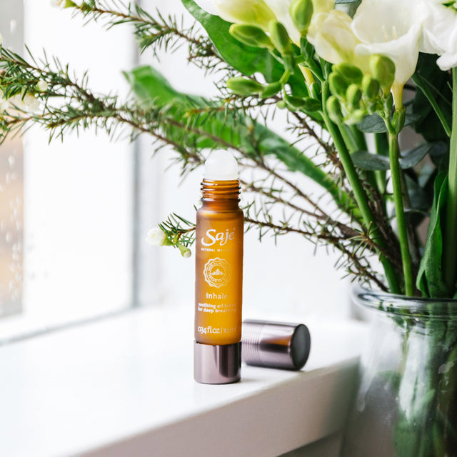 Inhale soothing oil blend roll-on 0.34 fl oz with lid removed placed beside a floral arrangement 